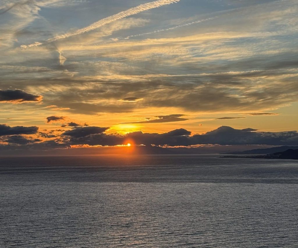 Sunset over the Mediterranean seen from the Cerro Gordo cliffs, the sun hiding behind clouds and vapour trails in the sky